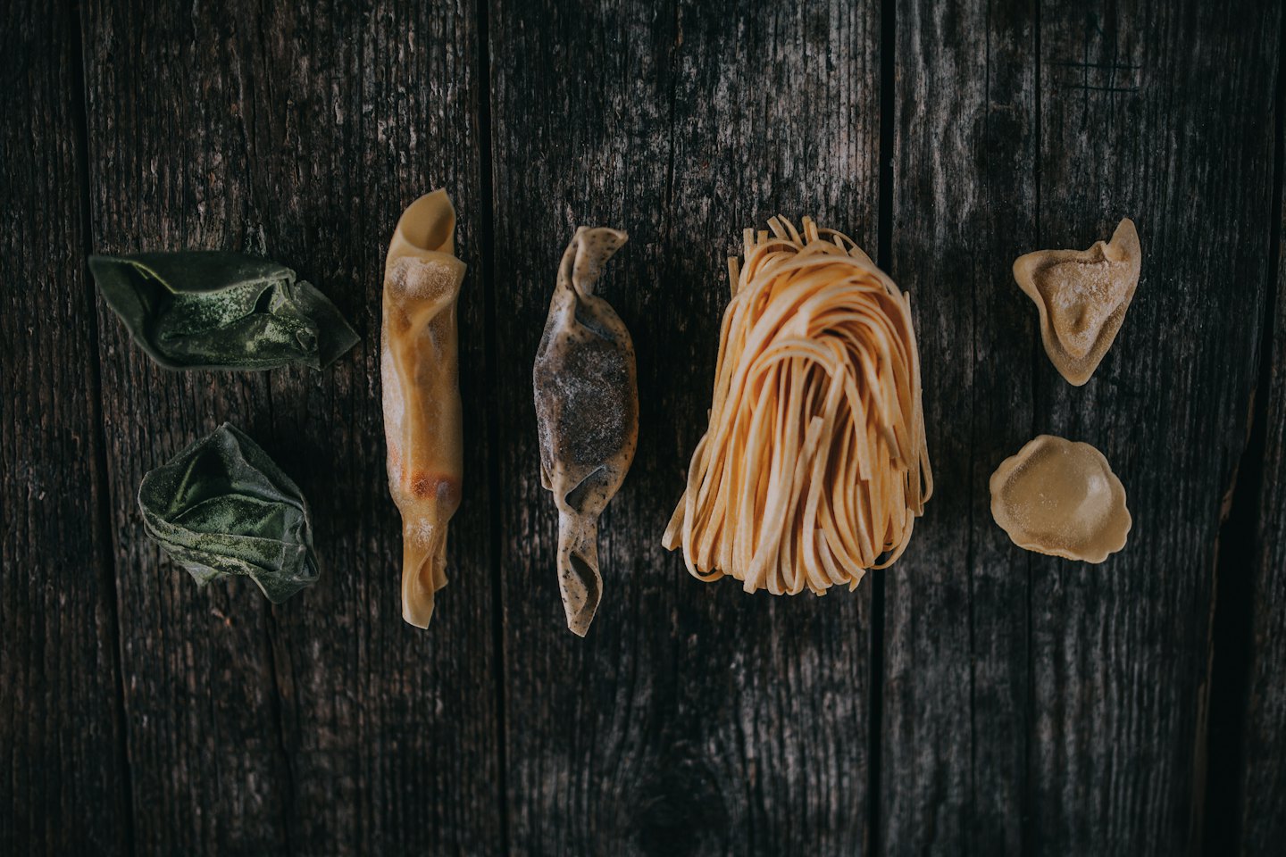 Vari tipi di pasta cruda disposti su una superficie di legno.