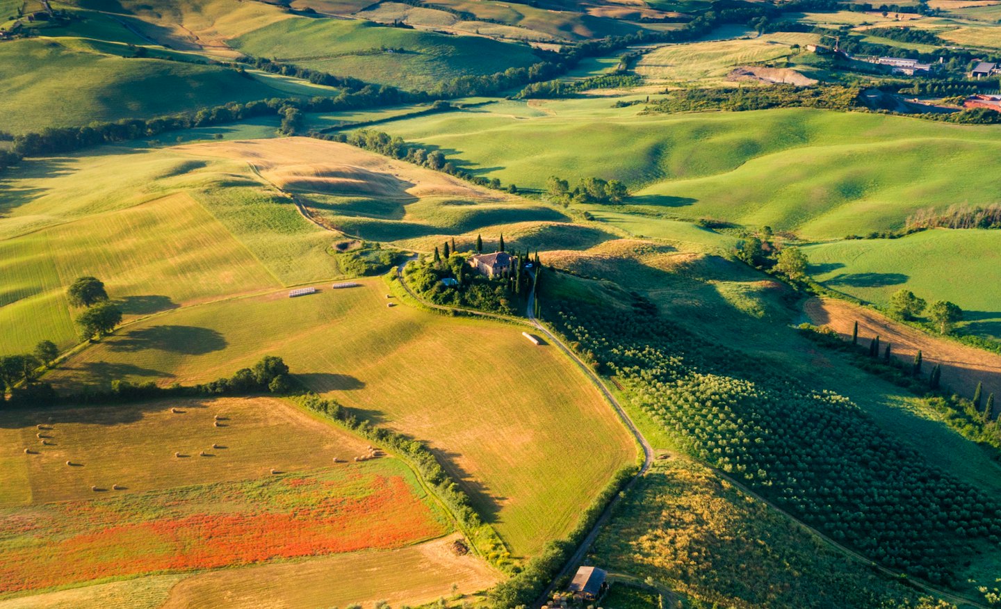Villa italiana illuminata dal sole su una collina circondata da colline verdi e campi dorati.